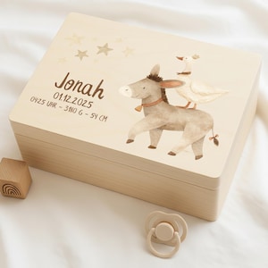 Puede incluir: Caja de recuerdo de madera clara con una ilustración de un burro y un ganso. La caja está personalizada con el nombre "Jonah" y los datos de nacimiento. Un bloque de madera y un chupete están junto a la caja.