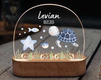 May include: A clear acrylic night light with a wooden base. The light features a blue and white watercolor illustration of a turtle, starfish, fish, and seaweed. The text "Levian 08.03.2024" is printed on the light.