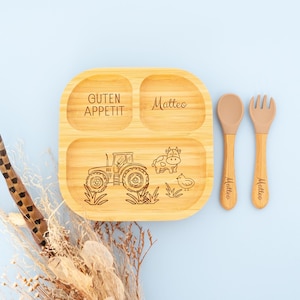 Może przedstawiać: Drewniany podzielony talerz z wzorem traktora, krowy i kurczaka. Na talerzu wygrawerowano słowa "Guten Appetit" i "Matteo". W zestawie znajduje się pasująca łyżka i widelec.