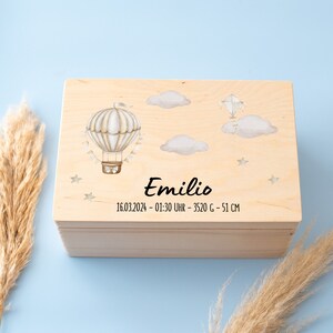 Peut inclure: Une boîte à souvenirs en bois avec une finition en bois clair. La boîte est décorée d'un ballon à air chaud et de nuages avec le nom "Emilio" et la date "16.03.2024 - 01:30 UHR - 3520 G - 51 CM" gravés sur le couvercle.