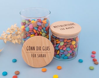 Pode incluir: Dois frascos de vidro cheios de doces coloridos, cada um com uma tampa de madeira. A tampa do frasco da esquerda diz "GÖNN DIR GLAS FÜR SARAH" e a tampa do frasco da direita diz "NOTFALLRESERVE FÜR MARKO".