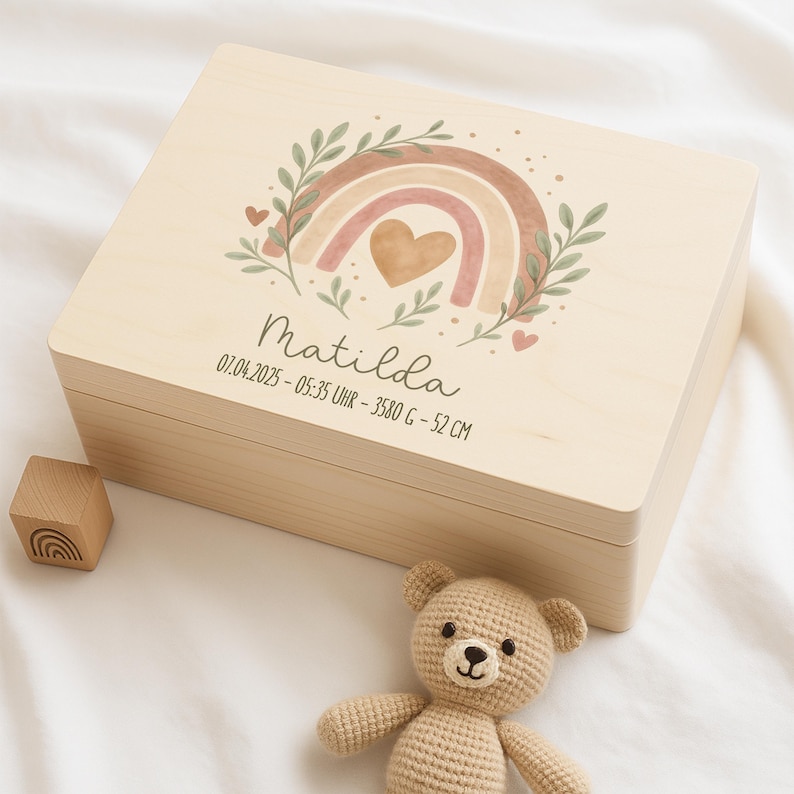 May include: A wooden keepsake box with a rainbow and heart design. The box is personalized with the name "Matilda" and the date "01.04.2025 - 05:35 Uhr - 3580 g - 52 cm".