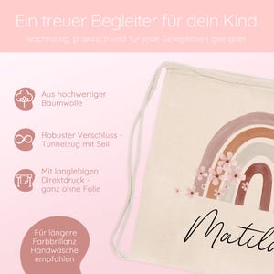 May include: A beige drawstring backpack with a watercolor rainbow design and the name "Matilda" in cursive. The bag features a sturdy drawstring closure and is made of high-quality cotton. The text "Ein treuer Begleiter f&uuml;r dein Kind" is at the top.