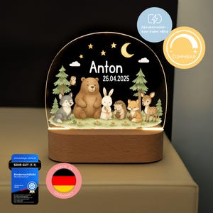 Könnte beinhalten: Eine Holz-Nachtlampe mit einer klaren Acrylkupel, die eine Waldszene mit einem Bären, Wolf, Kaninchen, Fuchs und Reh zeigt. Die Kuppel wird mit einem warmweißen Licht beleuchtet und der Name Anton sowie das Datum 26.04.2025 sind auf die Kuppel gedruckt. Die Nachtlampe ist batteriebetrieben und dimmbar.