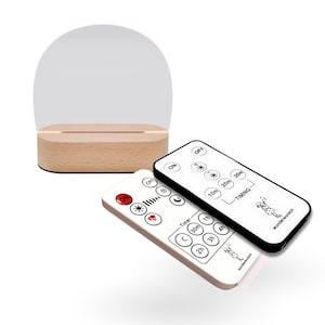 Op de afbeelding: Een houten basis met een helder, gebogen acryl paneel. Twee witte afstandsbedieningen met zwarte tekst en illustraties staan op de voorgrond. De afstandsbedieningen hebben knoppen voor timing en helderheidsregeling.