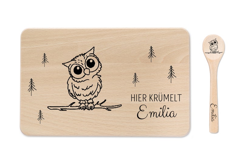 Op de afbeelding: Een houten snijplank met een schattig uil-ontwerp en de tekst "HIER KR&Uuml;MELT Emilia". Het wordt geleverd met een bijpassende houten lepel met hetzelfde uil-ontwerp en de naam "Emilia" erop gegraveerd.