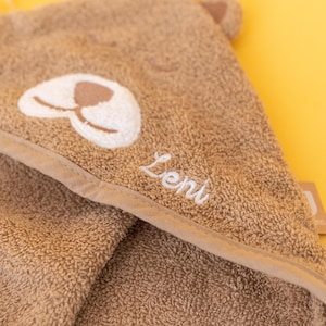 May include: A brown hooded towel with a white embroidered animal face and the name "Leni" stitched on the hood.