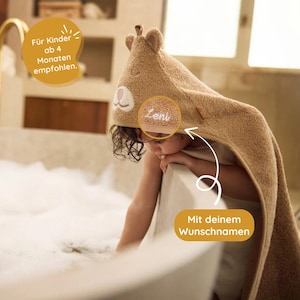 May include: A brown hooded towel with a bear face and the name "Leni" embroidered on it. The towel is being worn by a child in a bathtub. The text "F&uuml;r Kinder ab 4 Monaten empfohlen." is visible in the top left corner of the image. The text "Mit deinem Wunschnamen" is visible in the bottom right corner of the image.
