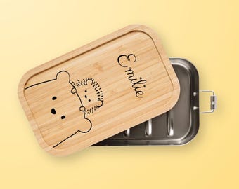 May include: A wooden lunchbox with a stainless steel interior. The lid features a hedgehog and bear design and the name "Emilie" is engraved on the lid.