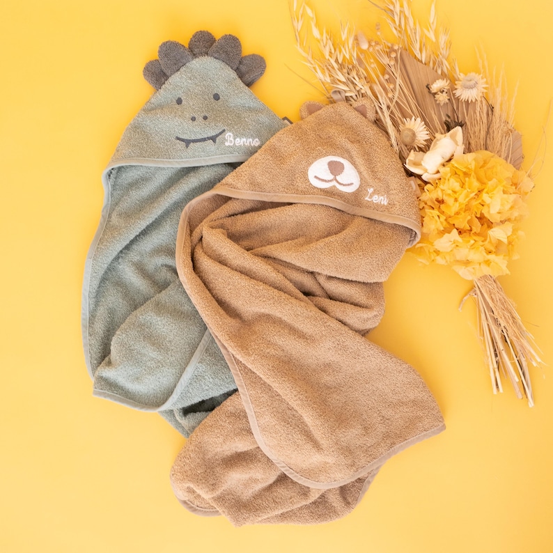 May include: Two hooded towels for babies, one green with a dinosaur face and the name "Benno" embroidered on it, and one brown with a bear face and the name "Levi" embroidered on it.