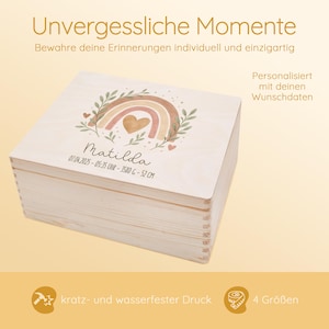 May include: A wooden keepsake box with a watercolor rainbow design, a heart, and the name Matilda. The box is personalized with the date, time, and measurements. The text "Unvergessliche Momente" is at the top of the image. The text "Personalisiert mit deinen Wunschdaten" is on the right side of the image. The text "kratz- und wasserfester Druck" is at the bottom left of the image. The text "4 Gr&ouml;&szlig;en" is at the bottom right of the image.