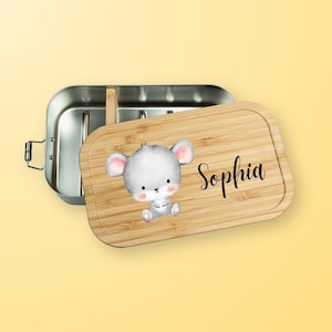 Könnte beinhalten: Edelstahl-Lunchbox mit Bambusdeckel. Der Deckel zeigt eine Aquarellillustration einer grauen Maus mit rosa Ohren und dem Namen "Sophia" in schwarzer Schrift. Die Lunchbox ist geöffnet.