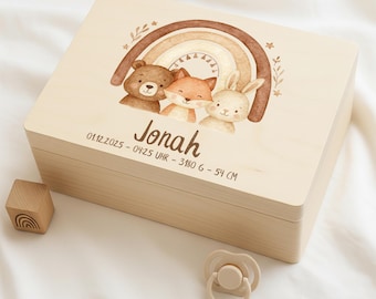 Puede incluir: Caja de recuerdos de madera clara con una ilustración de acuarela de un arcoíris y tres animales: un oso, un zorro y un conejo. El nombre "Jonah" está impreso debajo, junto con los detalles del nacimiento. Un bloque de madera y un chupete están al lado.