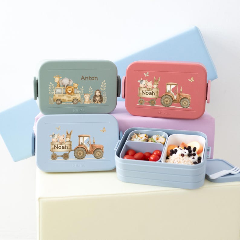 May include: Three blue, pink, and light blue lunch boxes with animal and tractor designs. The lunch boxes have the names Anton, Noah, and Noah on them. The light blue lunch box is open and has a compartment for food.