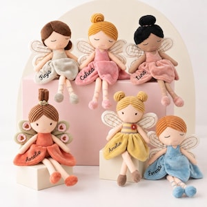 May include: Six plush fairy dolls with embroidered names on their skirts. Each doll features soft fabric wings, closed eyes, and distinct hair colors including brown, blonde, black, and ginger. The dolls wear dresses in sage, pink, orange, yellow, and blue.