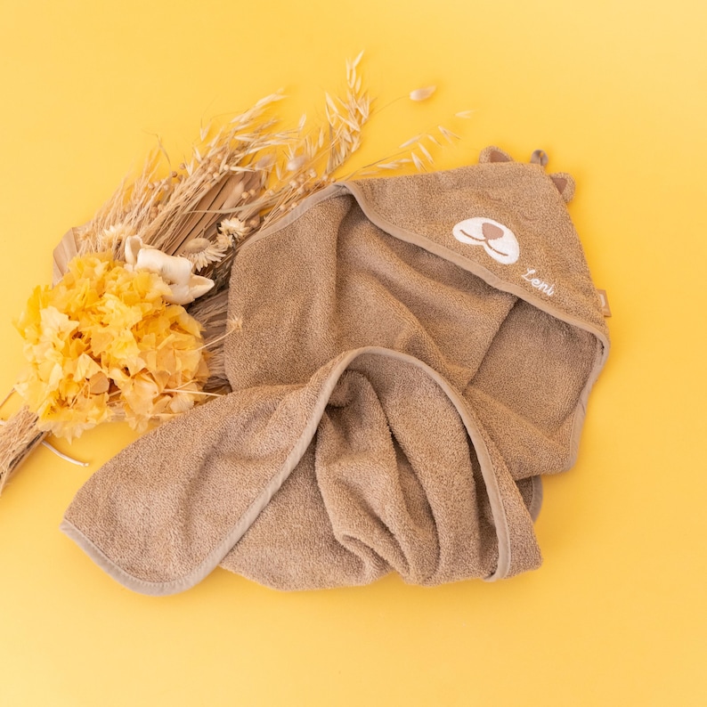 May include: A brown hooded towel with a cute bear face embroidered on the hood. The towel is made of soft, absorbent material and is perfect for drying a baby after bath time.