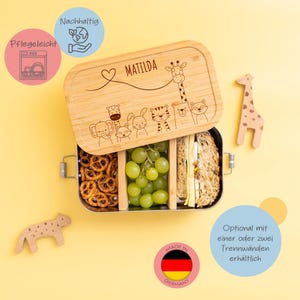 Könnte beinhalten: Eine Lunchbox aus Holz mit einem niedlichen Tierdesign und dem Namen "MATILDA" auf dem Deckel. Die Lunchbox ist in Deutschland hergestellt und mit optionalen Trennwänden erhältlich. Die Lunchbox ist gefüllt mit einem Sandwich, Trauben und Brezeln.
