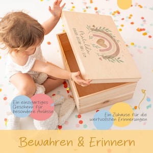 May include: A wooden keepsake box with a rainbow and floral design. The box is personalized with the name "Matilda" and the date "01.04.2025 - 05:35 UR - 35806 - 52CM". The box is open and a child is reaching inside. The text "Ein einzigartiges Geschenk f&uuml;r besondere Anl&auml;sse" is on the left side of the image and "Ein Zuhause f&uuml;r die wertvollsten Erinnerungen" is on the right side of the image. The text "Bewahren & Erinnern" is at the bottom of the image.