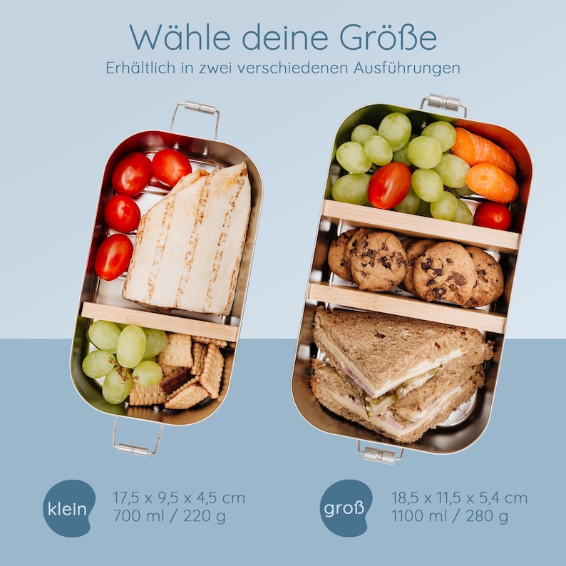 May include: Two stainless steel lunch boxes, one filled with tomatoes, a wrap, grapes, and crackers, the other with grapes, carrots, cookies, and sandwiches. The text reads "W&auml;hle deine Gr&ouml;&szlig;e" and size details.