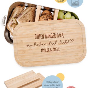 May include: A stainless steel lunch box with a bamboo lid. The lid is engraved with the text "GUTEN HUNGER PAPA, wir haben dich lieb!♡ MATILDA & AMELIE". The lunch box contains sandwiches, cookies, and grapes. Includes two small bamboo dividers.
