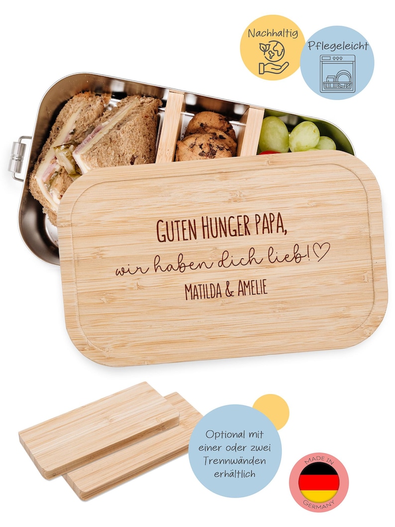 May include: A stainless steel lunch box with a bamboo lid. The lid is engraved with the text "GUTEN HUNGER PAPA, wir haben dich lieb!♡ MATILDA & AMELIE". The lunch box contains sandwiches, cookies, and grapes. Includes two small bamboo dividers.