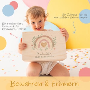 May include: A wooden keepsake box with a rainbow design and the name Matilda, birth date, weight, and length. The box is held by a young child.