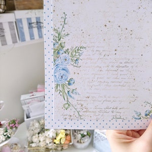 May include: A white card with a blue polka dot border and a watercolor illustration of blue flowers. The card has a handwritten message in gold ink.