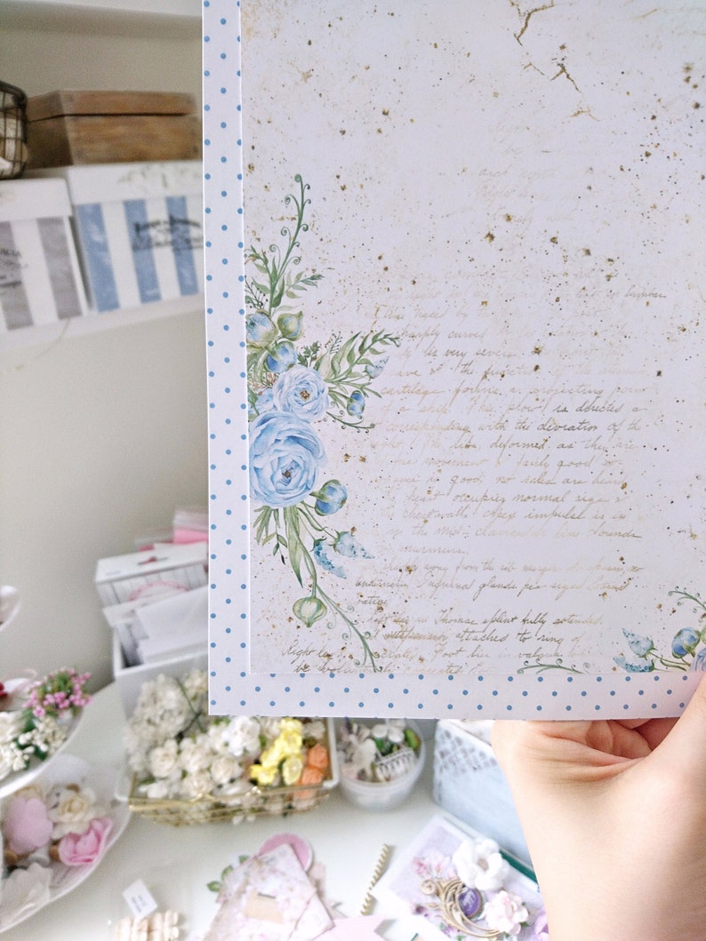 May include: A white card with a blue polka dot border and a watercolor illustration of blue flowers. The card has a handwritten message in gold ink.