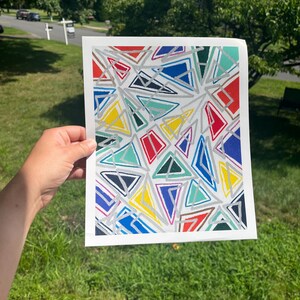 May include: A rectangular art print featuring a geometric pattern of various triangles in red, blue, yellow, teal, and dark green. The shapes are outlined with thick, textured silver lines against a white background, creating a mosaic-like effect.