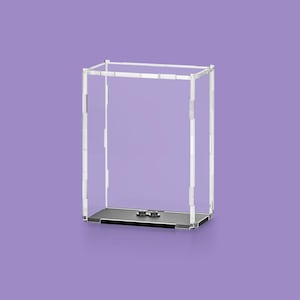 May include: A clear acrylic display case with a rectangular shape. The case has a black base and a clear top frame. The background is a solid purple color. The case is designed to showcase collectibles or other items.