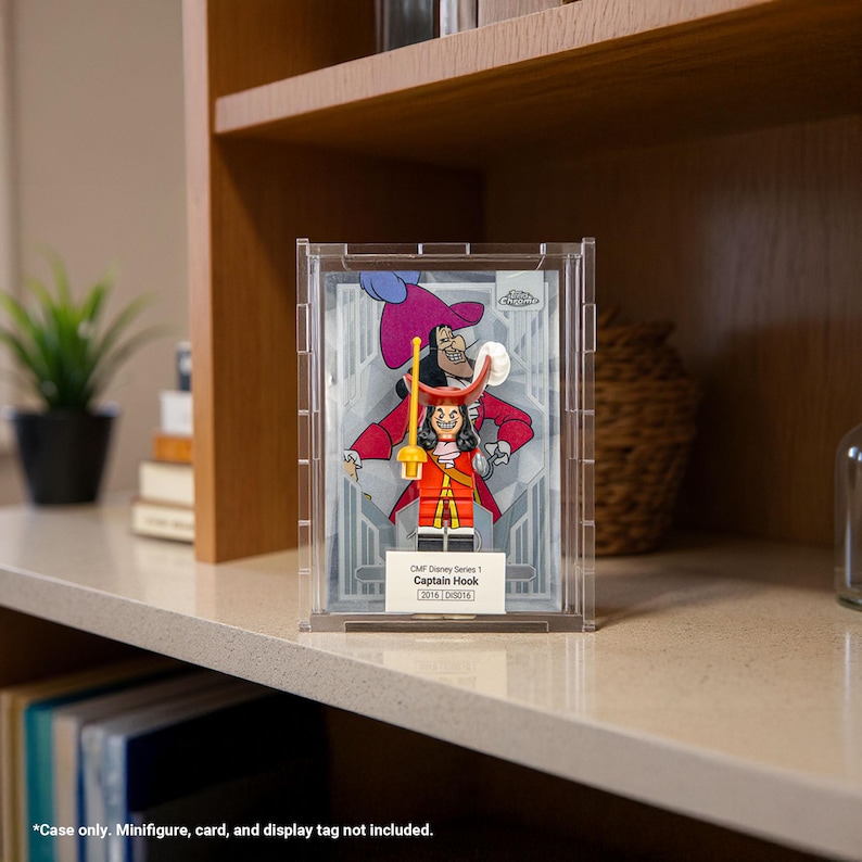 May include: A clear acrylic display case featuring a Captain Hook Lego minifigure. The minifigure is in a red coat, black pants, and a white wig. The case has the text "CMF Disney Series 1 Captain Hook".