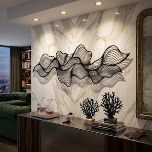 May include: Black metal wall art in a flowing, wave-like design. The artwork is mounted on a marble-effect wall. Decorative coral sculptures and decanters are displayed on a dark cabinet below.