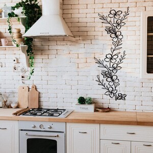 Puede incluir: Una cocina blanca con gabinetes blancos y un salpicadero de ladrillo blanco. Un dise&ntilde;o floral negro est&aacute; en la pared. Una campana extractora blanca est&aacute; sobre una estufa de gas. Una tabla de cortar de madera est&aacute; en la encimera.