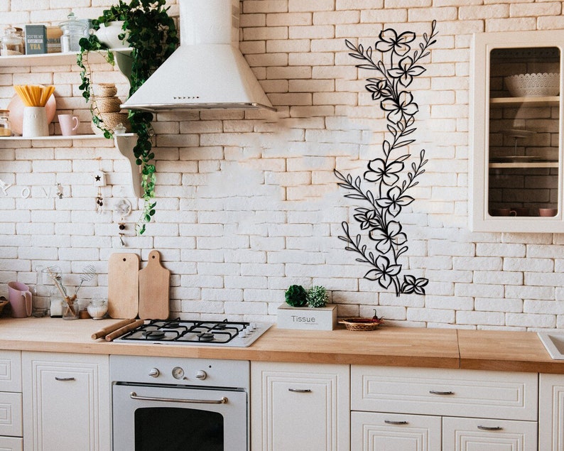 Puede incluir: Una cocina blanca con gabinetes blancos y un salpicadero de ladrillo blanco. Un dise&ntilde;o floral negro est&aacute; en la pared. Una campana extractora blanca est&aacute; sobre una estufa de gas. Una tabla de cortar de madera est&aacute; en la encimera.