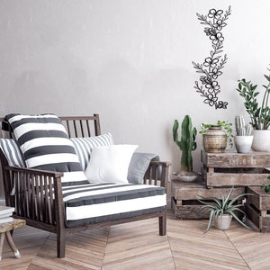 Puede incluir: Un sill&oacute;n a rayas con almohadas se encuentra en una habitaci&oacute;n con una pared de madera y una decoraci&oacute;n de pared floral de metal. Hay cajas de madera apiladas en el suelo con plantas en macetas.