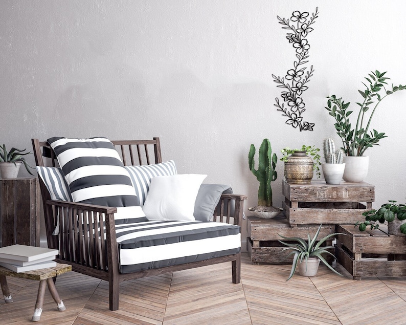 Puede incluir: Un sill&oacute;n a rayas con almohadas se encuentra en una habitaci&oacute;n con una pared de madera y una decoraci&oacute;n de pared floral de metal. Hay cajas de madera apiladas en el suelo con plantas en macetas.