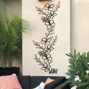Puede incluir: Pegatina de pared floral negra con un dise&ntilde;o vertical que presenta flores y hojas estilizadas. La pegatina se aplica a una pared blanca.