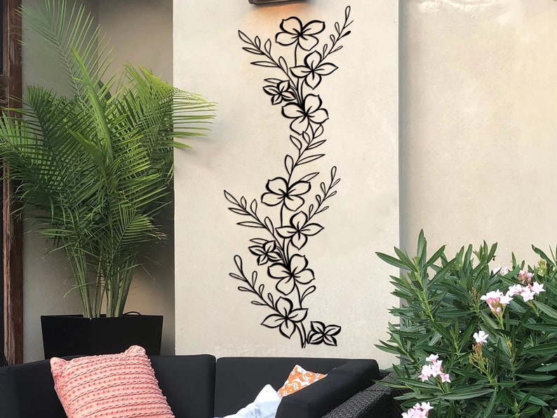 Puede incluir: Pegatina de pared floral negra con un dise&ntilde;o vertical que presenta flores y hojas estilizadas. La pegatina se aplica a una pared blanca.