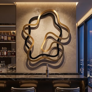 May include: A large wall sculpture featuring two intertwined, fluid, organic shapes in matte black and metallic gold. The sculpture is mounted on a textured light grey wall above a dark marble bar counter, creating a layered, three-dimensional effect.