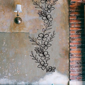 Puede incluir: Pegatina de pared floral negra con un dise&ntilde;o de vid, con m&uacute;ltiples flores y hojas. La pegatina se aplica a una pared texturizada de color marr&oacute;n claro.
