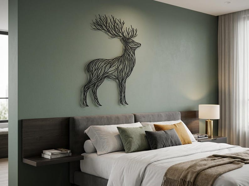 May include: A black metal deer wall art decorates a green wall above a bed with gray headboard and pillows. The deer is stylized with a line art design. The bed has white sheets and a brown blanket.