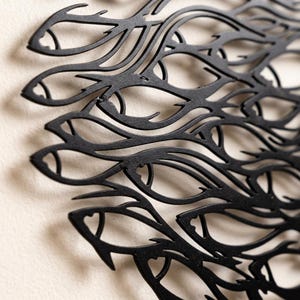 May include: A black metal wall art piece featuring a laser-cut design of a dense school of fish swimming in a unified direction. The intricate cutout pattern creates a silhouette of overlapping fish shapes with pointed fins and defined eyes.