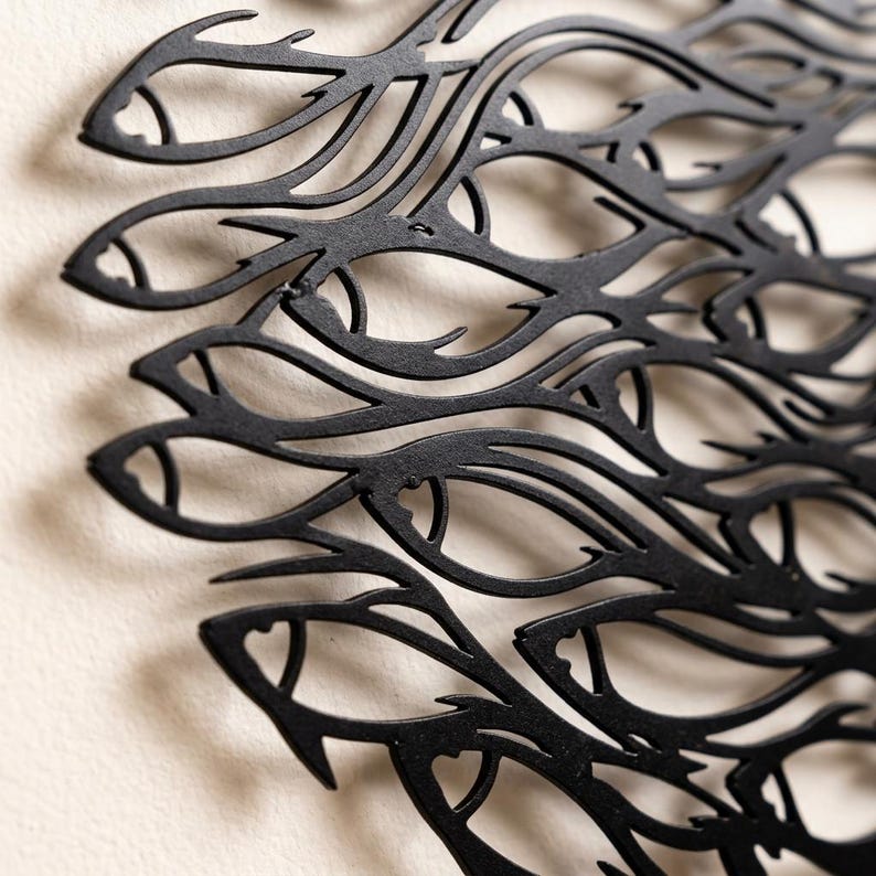 May include: A black metal wall art piece featuring a laser-cut design of a dense school of fish swimming in a unified direction. The intricate cutout pattern creates a silhouette of overlapping fish shapes with pointed fins and defined eyes.