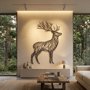 May include: A large, black metal deer wall art piece with intricate line detailing. The artwork is mounted on a light-colored wall, illuminated by spotlights. The room features a neutral color palette, a wooden coffee table, and large windows overlooking a forest.
