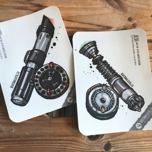 Puede incluir: Dos tarjetas ilustradas con sables de luz y objetos circulares. Un sable de luz es negro y gris con una hoja roja, el otro es plateado y gris con una hoja verde. Las tarjetas tienen el texto "JEDI NAY THE 4TH LIMITED EDITION" y "RIVERWALKER.CA".