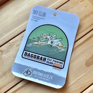 Può includere: Un caccia X-Wing Star Wars bianco e arancione sommerso in acqua con una lenza da pesca attaccata. L'adesivo è intitolato "Dagobah Fly Fishing Club" con il testo "Riverwalker.ca" in basso.