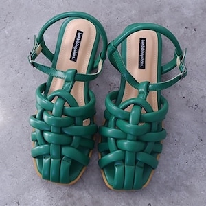 May include: A pair of green woven leather sandals with ankle straps and the brand name "beautifulaccessories" printed on the straps.