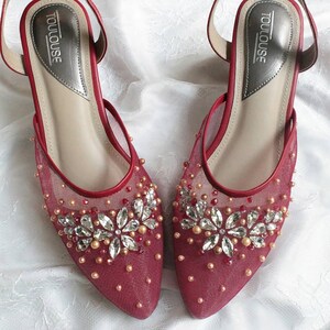 Puede incluir: Un par de zapatos de novia de malla roja con adornos plateados y dorados. Los zapatos tienen punta puntiaguda y tacón bajo. El nombre de la marca "TOULOUSE" está impreso en la plantilla.