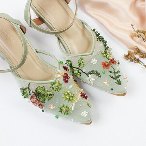 K&ouml;nnte beinhalten: Ein Paar hellgr&uuml;ne Schuhe mit Absatz, zarte florale Stickerei und Perlenbesatz. Die Schuhe haben eine spitze Zehenpartie und einen Kn&ouml;chelriemen.