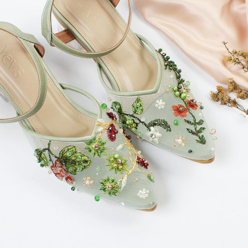 K&ouml;nnte beinhalten: Ein Paar hellgr&uuml;ne Schuhe mit Absatz, zarte florale Stickerei und Perlenbesatz. Die Schuhe haben eine spitze Zehenpartie und einen Kn&ouml;chelriemen.